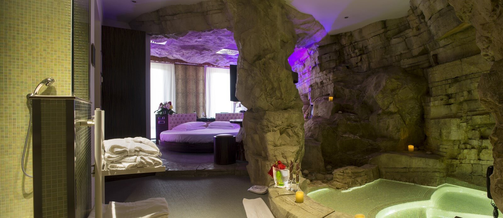 Motel K Wellness Suite Grotta Verde Motel K Wellness Suite Grotta Verde vista dai servizi, minipiscina idromassaggio con servizio candele in suite, bottiglia di champagne a bordo piscina, sullo sfondo si intravede il letto matrimoniale rotondo, camera a tema marina di andrano